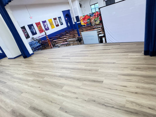 New wood style floors installed on a stage. Stage is raised up and the view overlooks the school cafeteria tables in rows. 